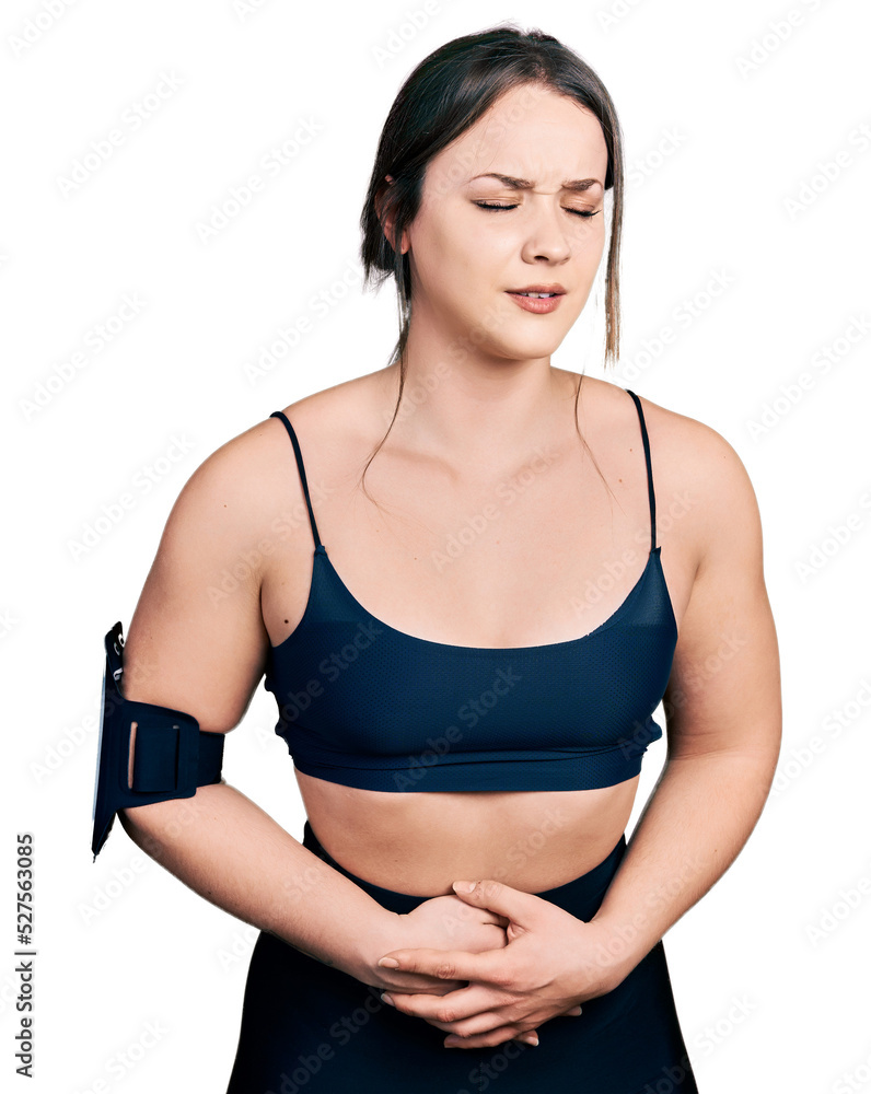 Young hispanic woman wearing sportswear with hand on stomach because nausea, painful disease feeling unwell. ache concept. Young hispanic woman wearing sportswear with hand on stomach because nausea, painful disease feeling unwell. ache concept.