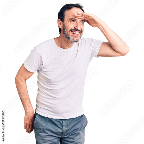 Middle age handsome man wearing casual t-shirt very happy and smiling looking far away with hand over head. searching concept.