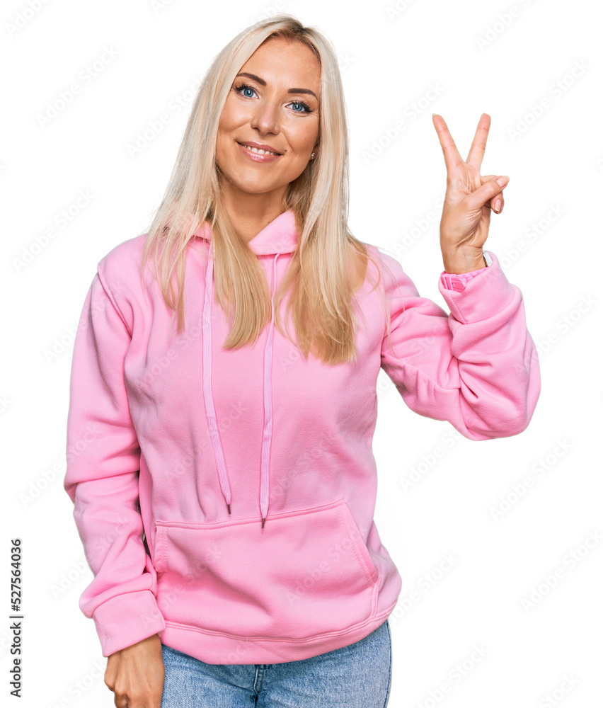 Young blonde woman wearing casual sweatshirt smiling looking to the camera showing fingers doing victory sign. number two. Young blonde woman wearing casual sweatshirt smiling looking to the camera showing fingers doing victory sign. number two.