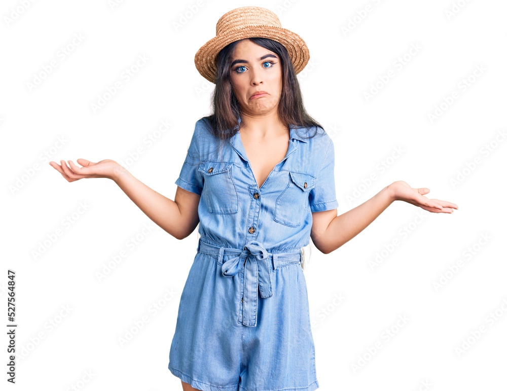 Brunette teenager girl wearing summer hat clueless and confused expression with arms and hands raised. doubt concept. Brunette teenager girl wearing summer hat clueless and confused expression with arms and hands raised. doubt concept.