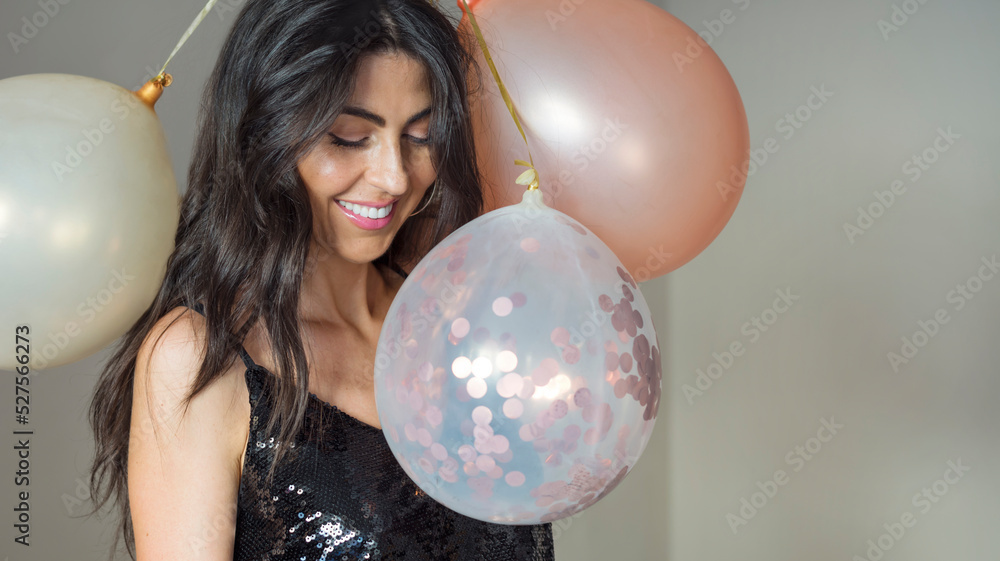 Fototapeta premium Beautiful woman in black shiny dress holding party balloons and smiling . Portrait with copy space 