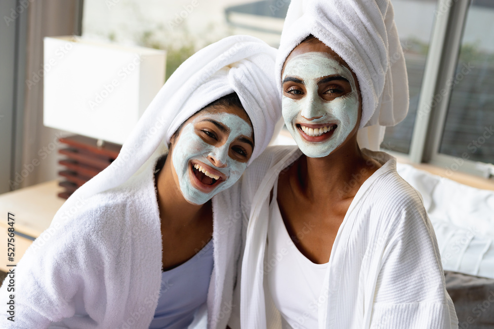 Portrait of smiling biracial mother and daughter with facial masks wearing bathrobes at home Portrait of smiling biracial mother and daughter with facial masks wearing bathrobes at home