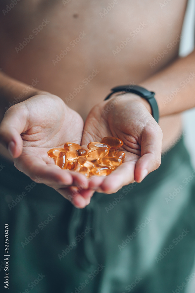 Obraz premium A handful of vitamins in the hands of a young guy. Bright Omega-3 capsules. Medicinal product of animal origin. Fish oil source of vitamins A and D