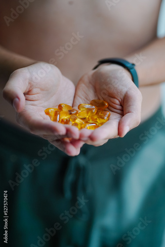 A handful of food suplements in the hands of a young guy in the form of heart. Bright Omega-3 capsules. Medicinal product of animal origin for healthy lifestyle. Fish fat source of vitamins A and D