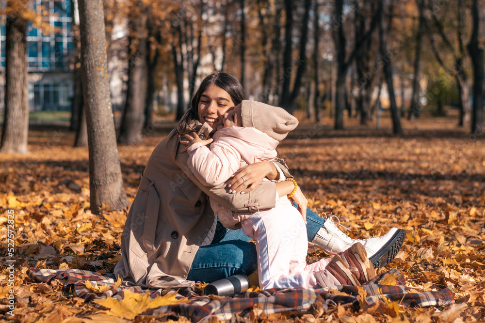 Happy dark-haired young mother and daughter hug and have fun at a picnic in the autumn park on a sunny day.Family and autumn concept. Happy dark-haired young mother and daughter hug and have fun at a picnic in the autumn park on a sunny day.Family and autumn concept.