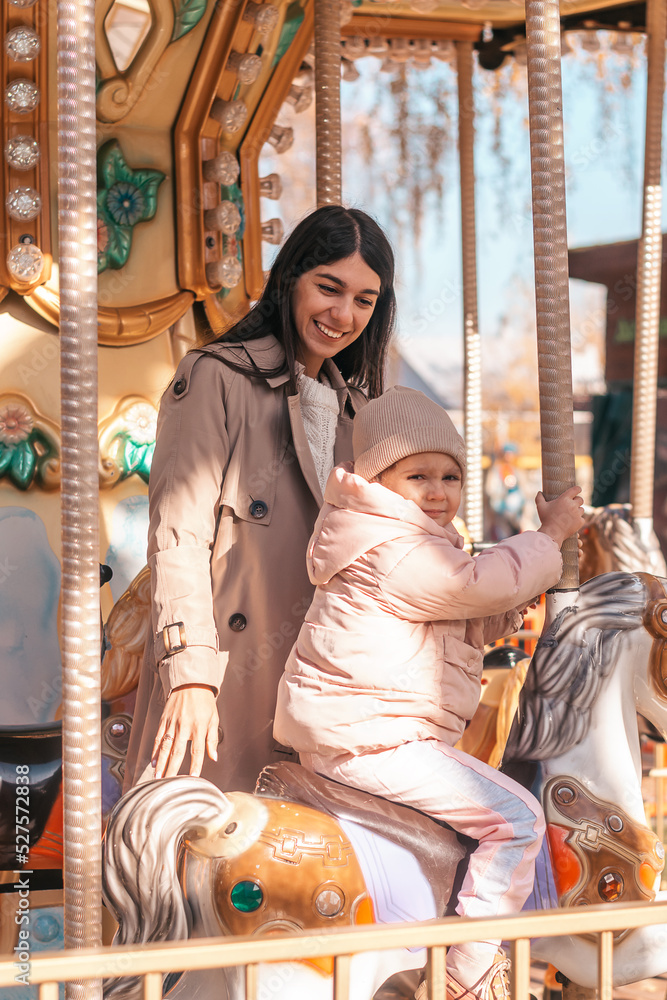 Happy dark-haired young mother and daughter having fun in an amusement park on an autumn day.Family concept.Selective focus.