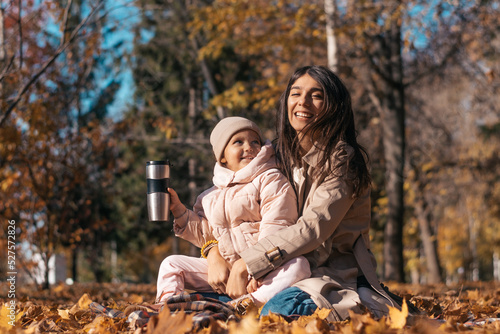 Happy dark-haired young mother and daughter having a picnic in an autumn park on a sunny day.Family and autumn concept. © Tatyana