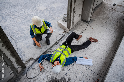 Accident at work, an Asian engineer or electrician is electrocuted to the ground. A colleague engineer rushed in for help or assistance. Concept of accident at a construction site.