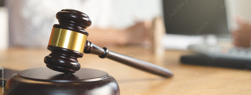 Close up view of auction hammer on the desk in lawyer office and lawyer writing document as background.