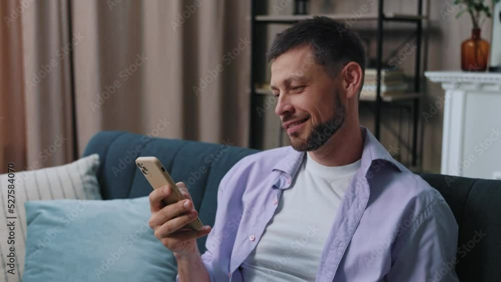 Portrait smiling happy young man use phone sitting on sofa at home. Communication businessman chatting scrolling social media. Close up. Portrait. Slow motion Portrait smiling happy young man use phone sitting on sofa at home. Communication businessman chatting scrolling social media. Close up. Portrait. Slow motion