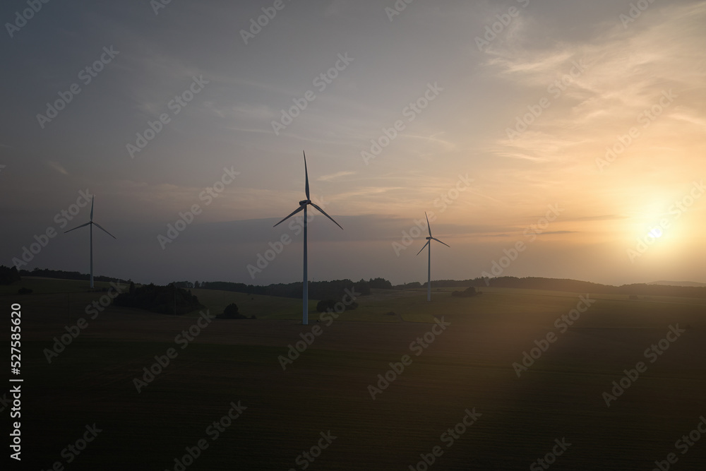 Obraz premium Aerial, scenic view of wind power plant silhouette against sunset. Aerial, drone inspection of three wind-powered electrical generators.