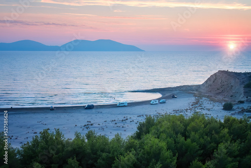 Aerial view, campervans and travellers, free camping on sandy beach against red sunset sky, van life holiday, summer, active people traveling concept. Albania