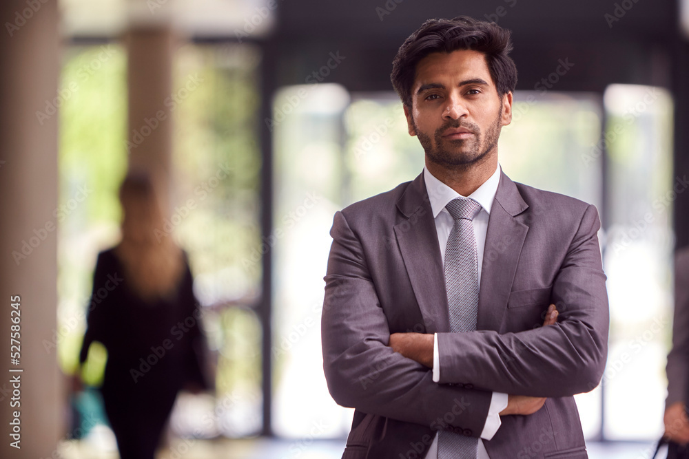 Portrait Of Businessman Standing In Lobby Of Busy Modern Office Building
