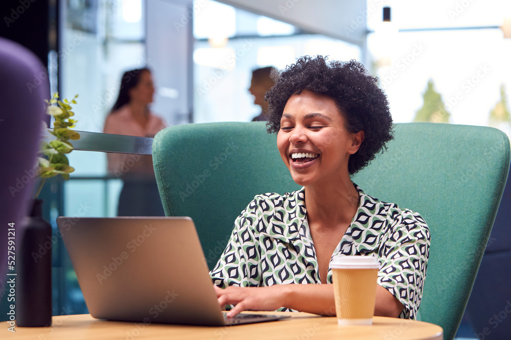 Businesswoman Using Laptop Working At Table In Breakout Seating Area Of Office Building Businesswoman Using Laptop Working At Table In Breakout Seating Area Of Office Building