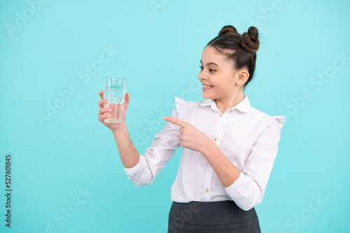 Teenager girl drinking water from glass on blue background. Daily life health. Drink water for health care and body balance. Thirsty kid, dehydration.