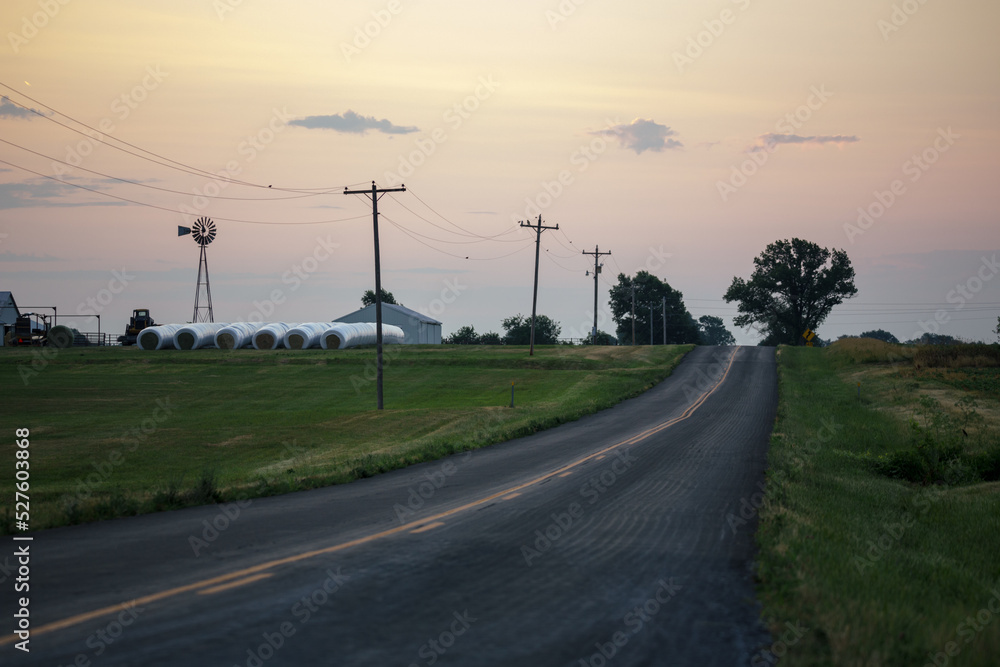 Fototapeta premium Sunset over rural farm with power lines and windmill