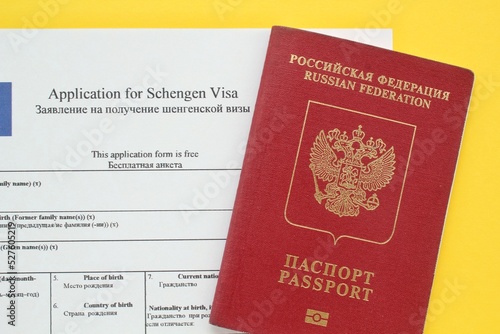Schengen visa application form in English and Russian language and passport on yellow background. Prohibition and suspension of visas for tourists to travel to European Union and Baltic States concept