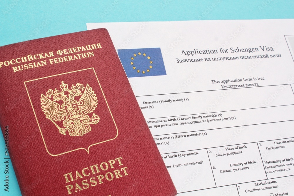 Schengen visa application form in English and Russian language and passport on blue background. Prohibition and suspension of visas for tourists to travel to European Union and Baltic States concept Schengen visa application form in English and Russian language and passport on blue background. Prohibition and suspension of visas for tourists to travel to European Union and Baltic States concept