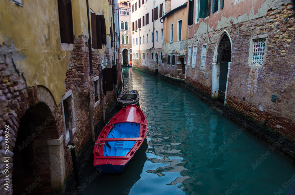 Una piccola imbarcazione rossa e blu ormeggiata in uno stretto canale di Venezia