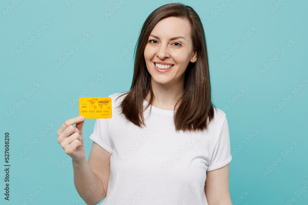 Young smiling happy caucasian woman 20s she wear white t-shirt hold in hand mock up of credit bank card isolated on plain pastel light blue cyan background studio portrait. People lifestyle concept. Young smiling happy caucasian woman 20s she wear white t-shirt hold in hand mock up of credit bank card isolated on plain pastel light blue cyan background studio portrait. People lifestyle concept.