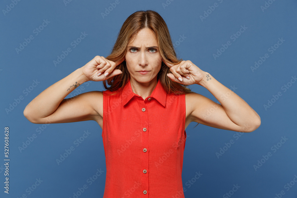 Young sad caucasian woman 30s she wear red dress cover ears with hands fingers do not want to listen scream isolated on plain dark royal navy blue background studio portrait. People lifestyle concept. Young sad caucasian woman 30s she wear red dress cover ears with hands fingers do not want to listen scream isolated on plain dark royal navy blue background studio portrait. People lifestyle concept.