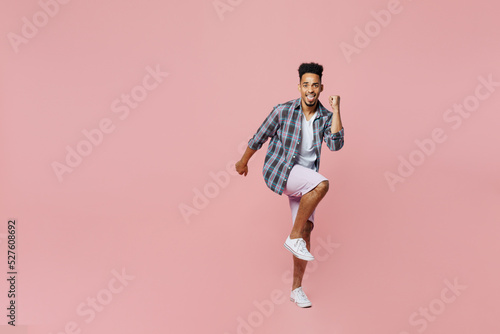 Full body young man of African American ethnicity 20s wear blue shirt doing winner gesture celebrate clenching fists say yes isolated on plain pastel light pink background People lifestyle concept.