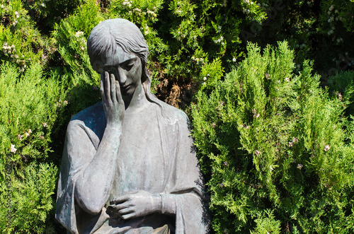 Primo piano di una statua in bronzo di una donna dolente su una tomba del cimitero maggiore di Milano