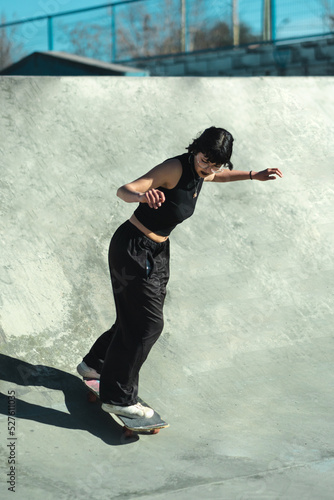 Gothic skater girl riding her skateboard on the of skate park bowl concrete.