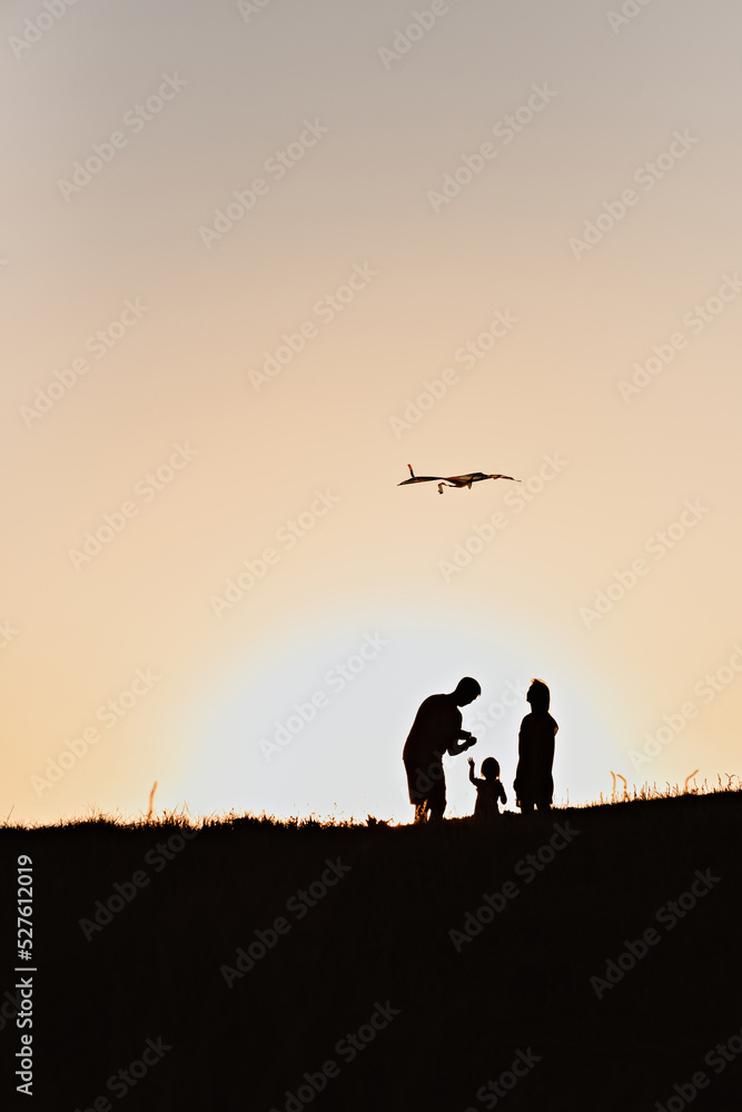 Fototapeta premium Silhouettes of a family flying a kite at sunset.