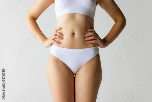 Close-up hips, belly, chest. Female tanned body of young woman in white underwear isolated on gray background. Natural beauty concept.