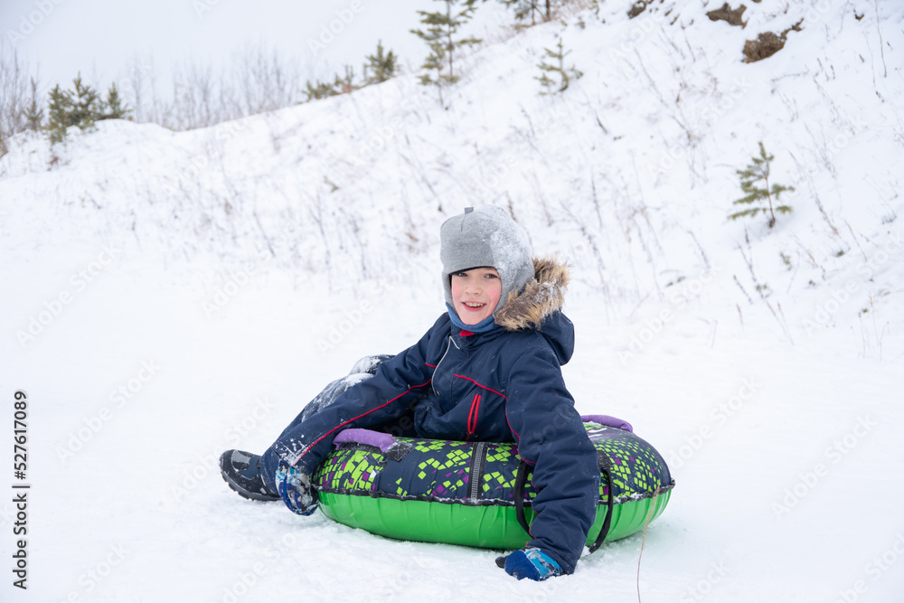 Happy smiling little boy slide down the ice slide, sits on an inflatable tubing. Cute little happy child having fun outdoors in winter on sledge. family winter time.