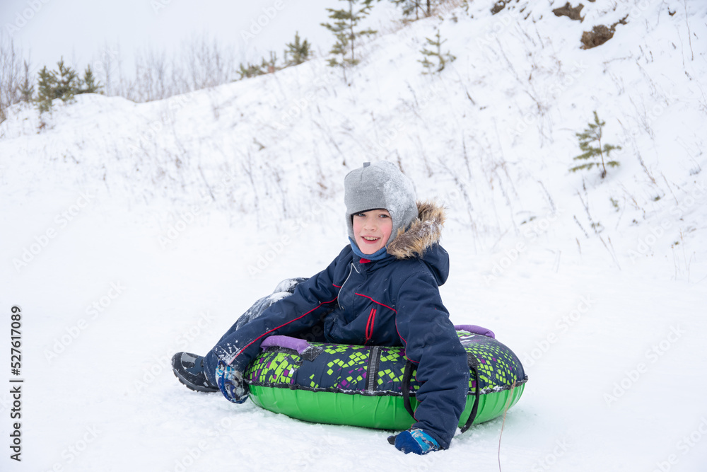 Happy smiling little boy slide down the ice slide, sits on an inflatable tubing. Cute little happy child having fun outdoors in winter on sledge. family winter time. Happy smiling little boy slide down the ice slide, sits on an inflatable tubing. Cute little happy child having fun outdoors in winter on sledge. family winter time.