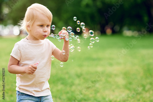 Cute caucasian blond chill girl blowing soap bubbles in summer park outdoors and have fun. Happy childhood concept
