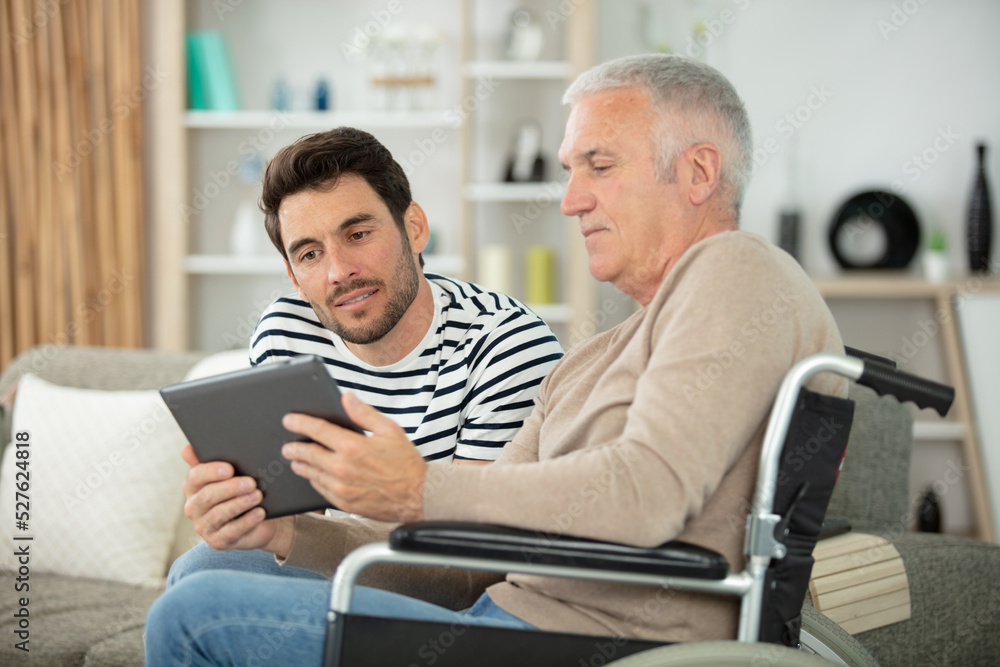 smiling son and father in wheelchair with tablet smiling son and father in wheelchair with tablet