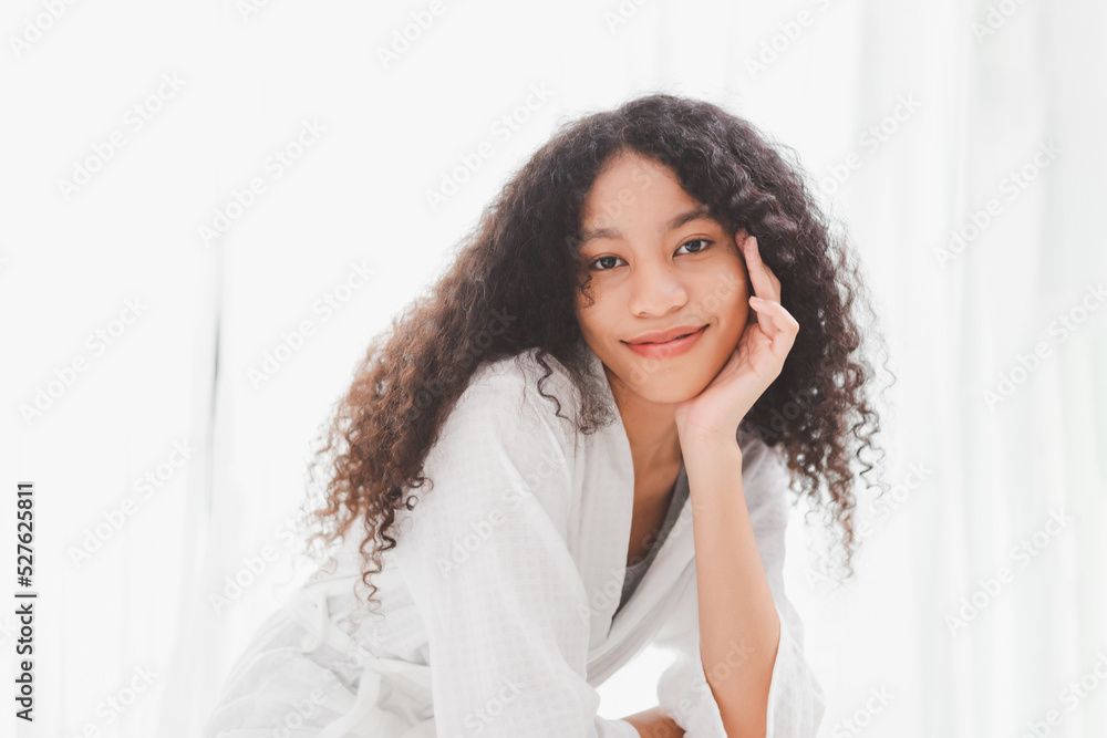 Young Makeup free face Mixed race African American woman wearing bathrobe sitting on the bed in bed room at home. Attractive happy lady with healthy no make up bare skin face. Young Makeup free face Mixed race African American woman wearing bathrobe sitting on the bed in bed room at home. Attractive happy lady with healthy no make up bare skin face.