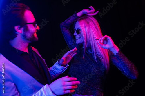 Stylish coupe in sunglasses dancing isolated on black with colorful lighting.
