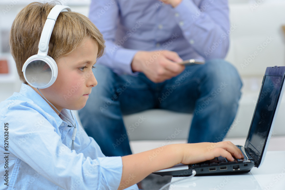 Boy wearing headphones on laptop, man holding cellphone Boy wearing headphones on laptop, man holding cellphone