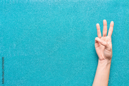 three points woman hand gesture on glitter turquoise background coming out from the side