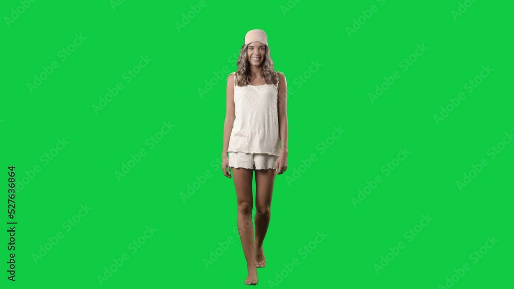 Happy young woman in pajamas walking and looking at camera with sleep eye mask. Full body isolated on green screen background Happy young woman in pajamas walking and looking at camera with sleep eye mask. Full body isolated on green screen background