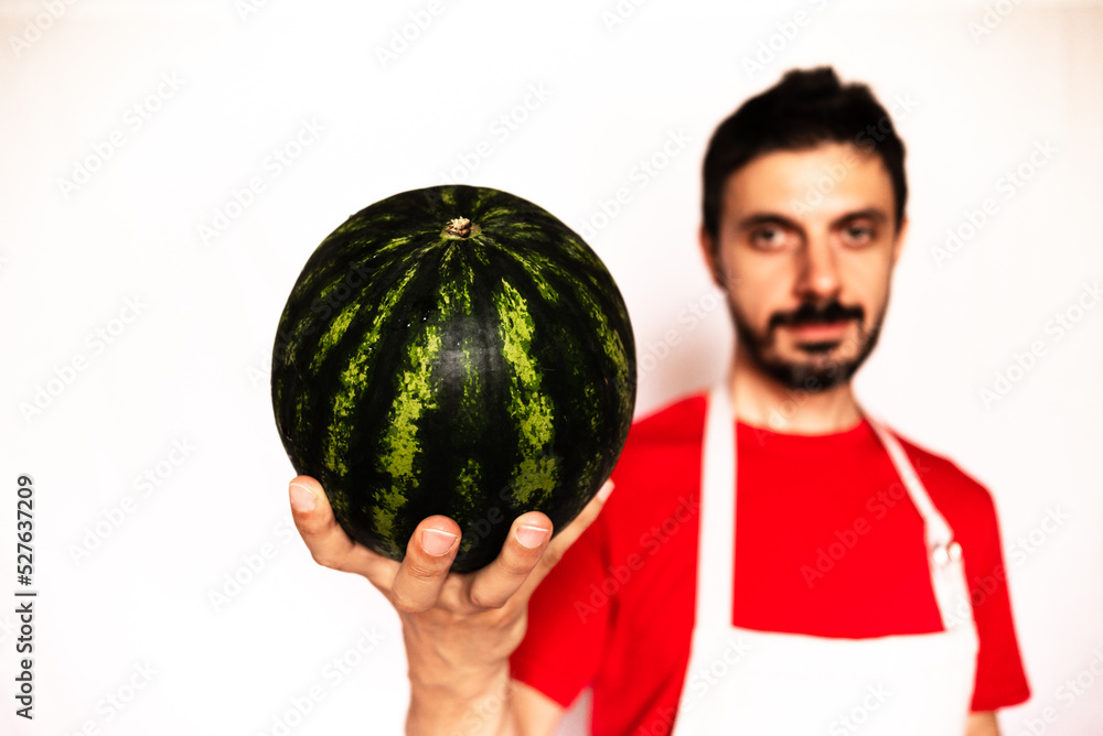 Caucasian man holds a watermelon in his hand. Healthy food for diet, man with red t-shirt on out of focus white background.