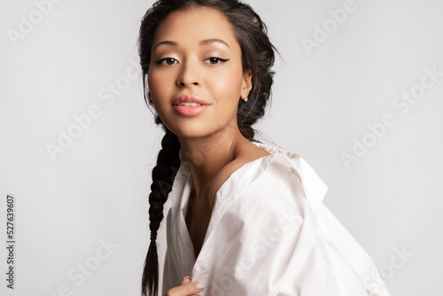 Canvas Print Beautiful biracial  girl wearing white shirt with healthy glowing skin, perfect make up smiling, posing on gray studio background with copy space for advertising