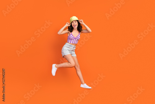 Fototapeta Naklejka Na Ścianę i Meble -  Full size photo of brunette impressed lady jump wear cap top shorts shoes isolated on orange color background
