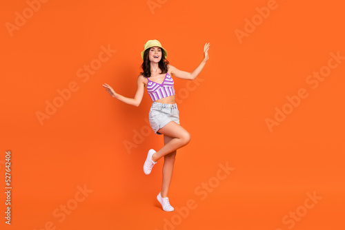 Full length photo of brunette crazy lady dance wear hat top jeans shorts shoes isolated on orange color background