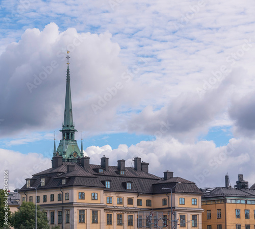 Facades of old 1700s houses and a church tower in the old town Gamla Stan a sunny day with cumulus clouds in Stockholm