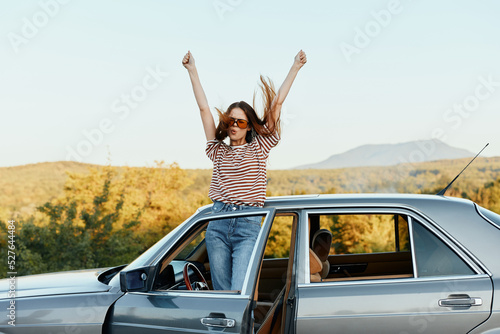 Happy woman traveler climbed on the car and spread her arms smiling happily. looks at the nature around. Lifestyle in travel and joy