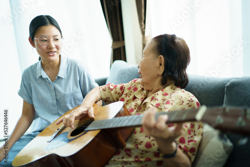 Asian elder woman playing an acoustic guitar and let her granddaughter taking a video on smartphone.