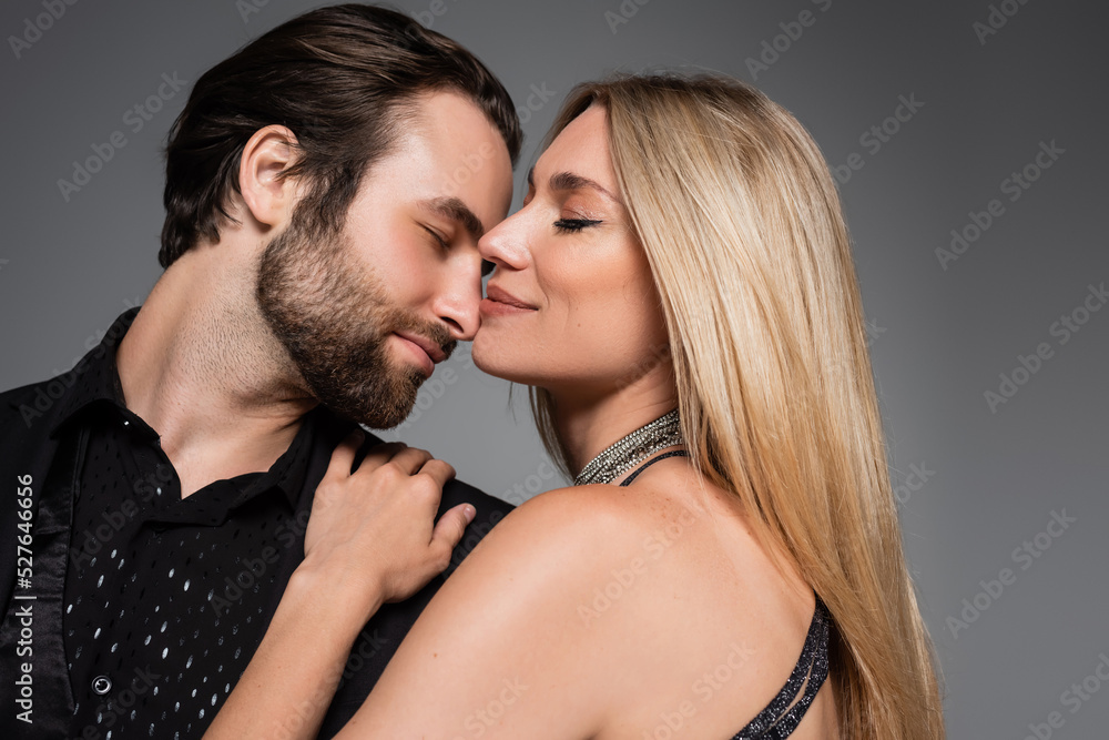 Side view of stylish blonde woman hugging bearded boyfriend isolated on grey.