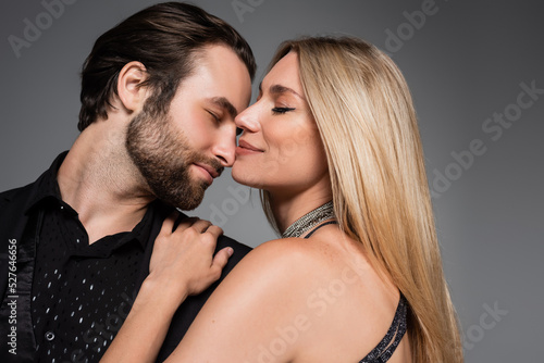 Side view of stylish blonde woman hugging bearded boyfriend isolated on grey.