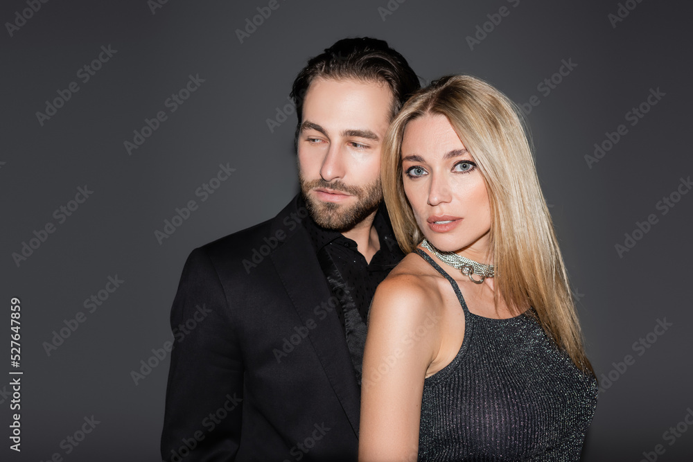 Bearded man in jacket standing near blonde girlfriend isolated on grey. Bearded man in jacket standing near blonde girlfriend isolated on grey.