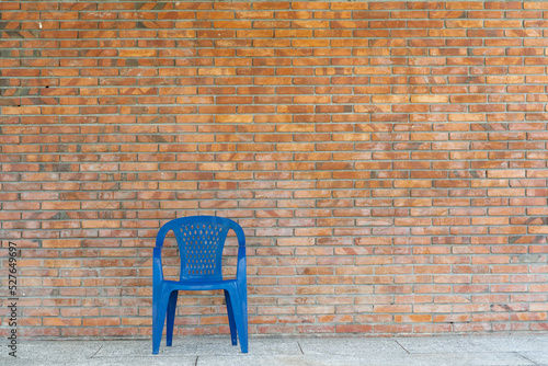 Single blue plastic chair in front of clay brick wall 
